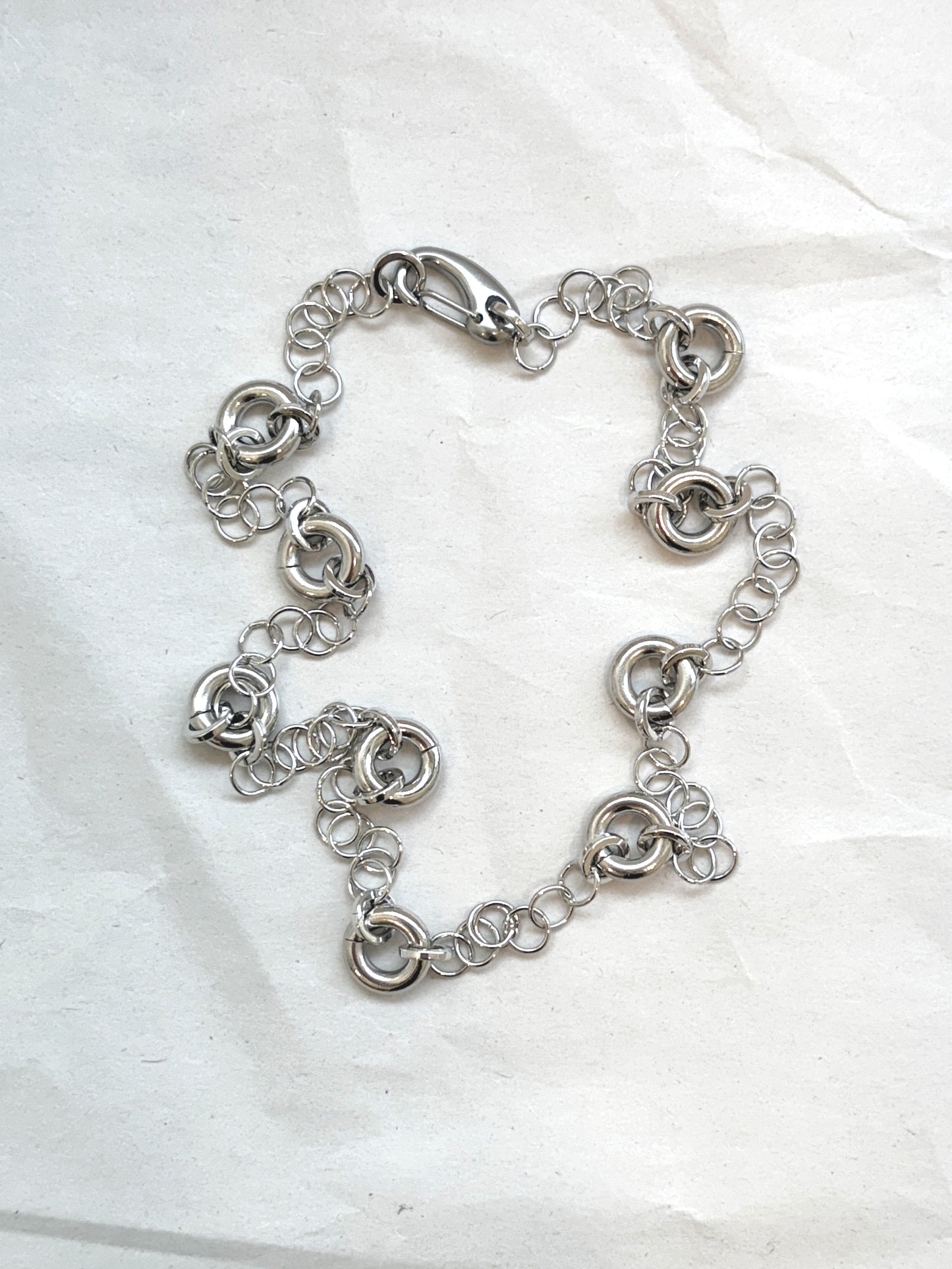 Delicate silver cable chain necklace with circular link accents, laid flat on a neutral background.