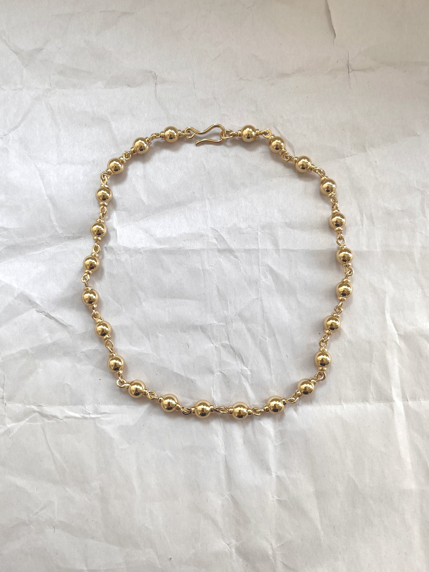 Laura Lombardi gold Suona beaded necklace on a white paper background.