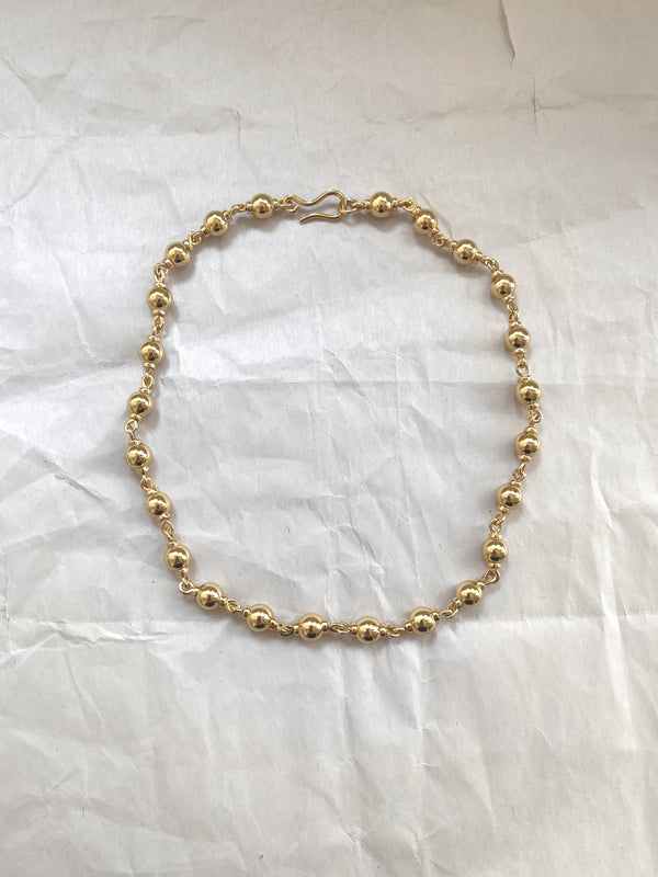 Laura Lombardi gold Suona beaded necklace on a white paper background.