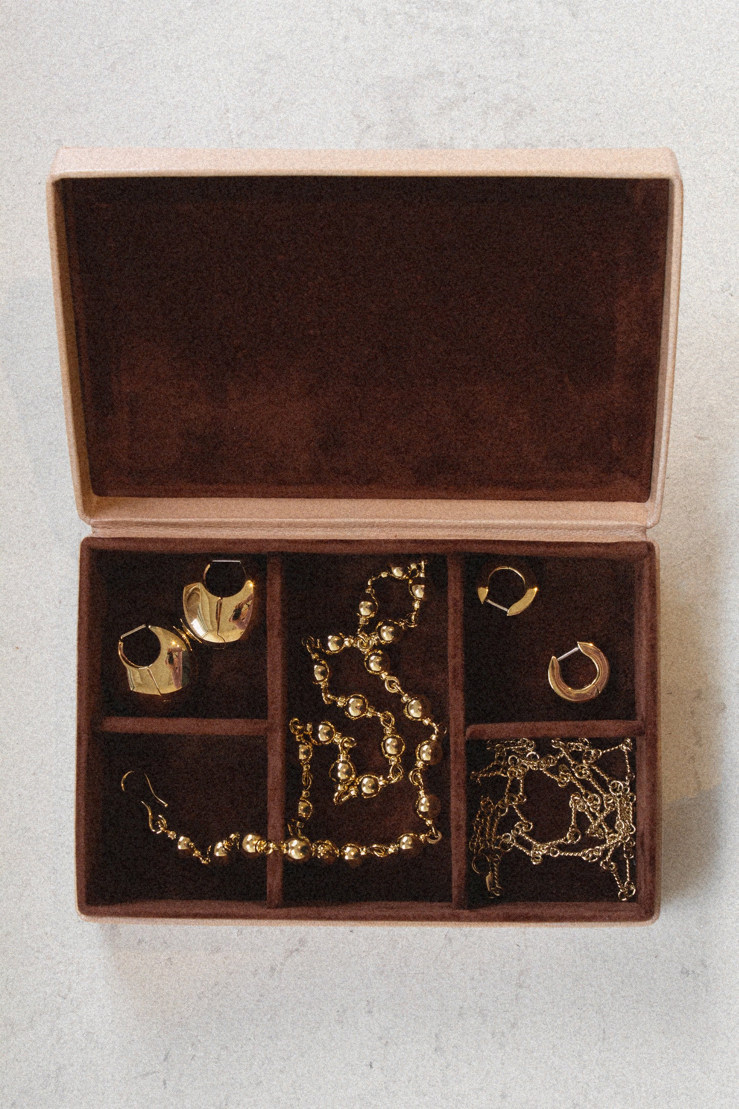 Laura Lombardi beige jewelry box with brown plush lining with gold necklaces and earrings inside.