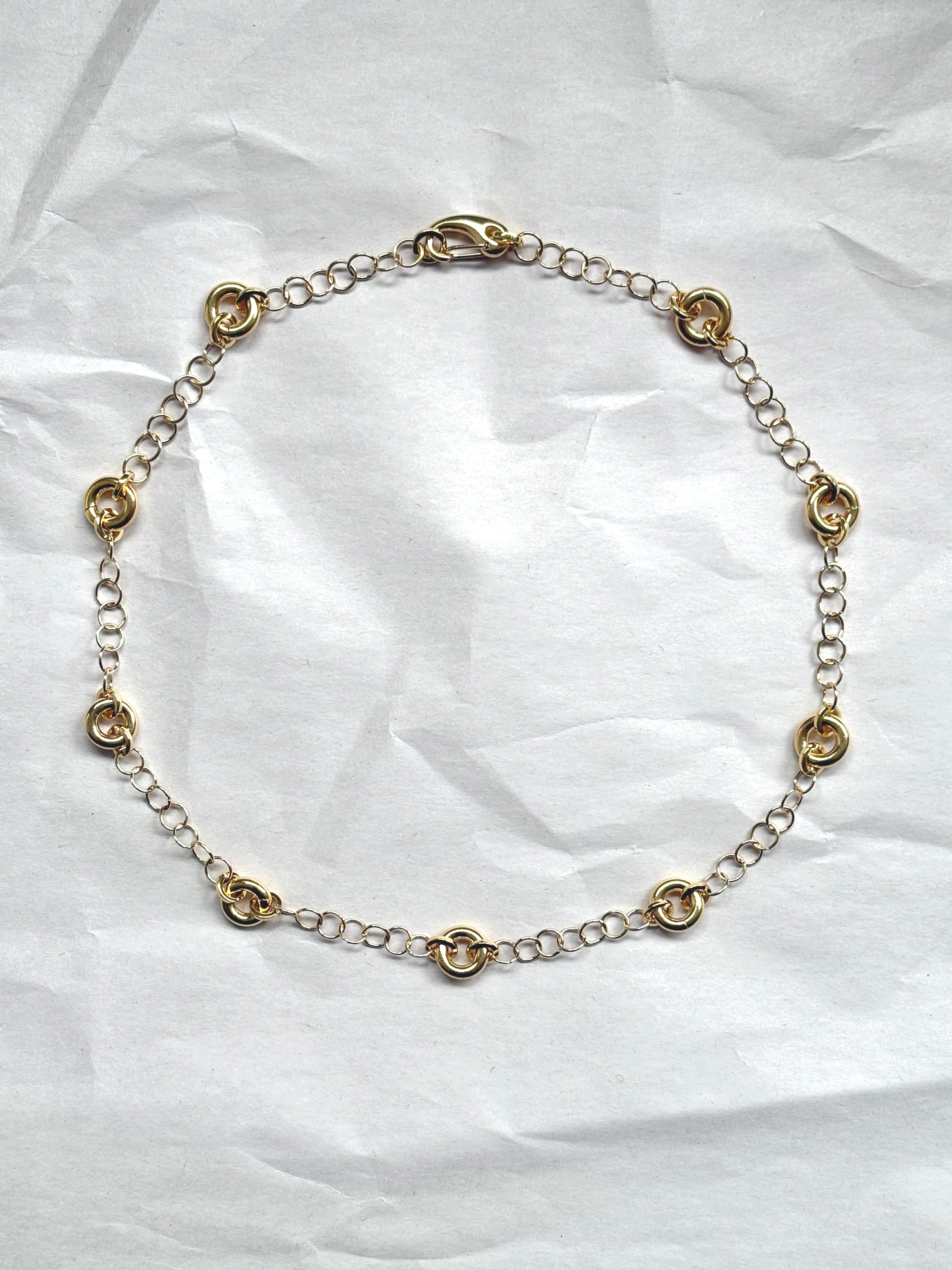Delicate gold cable chain necklace with circular link accents, laid flat on a neutral background.