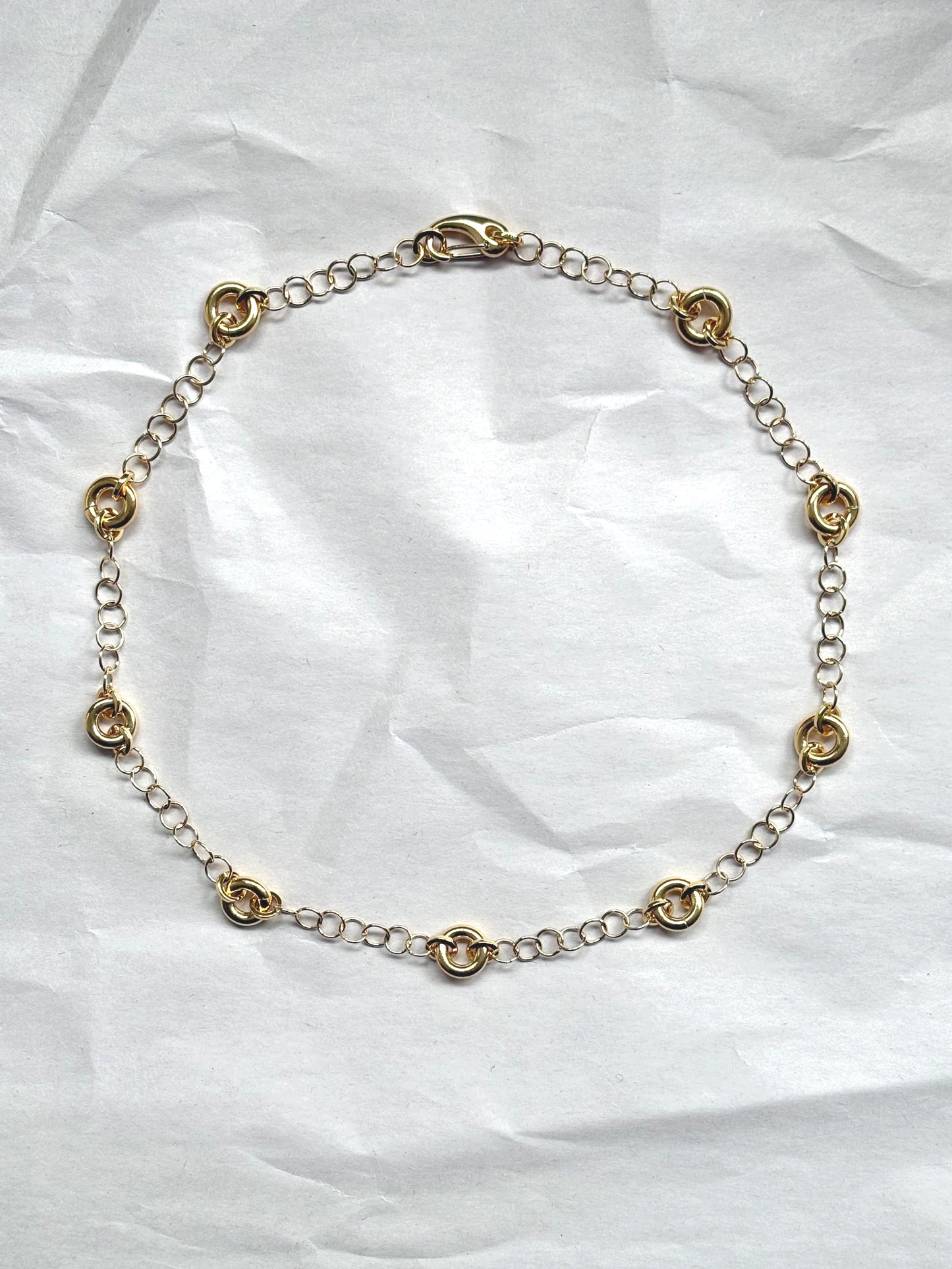 Delicate gold cable chain necklace with circular link accents, laid flat on a neutral background.