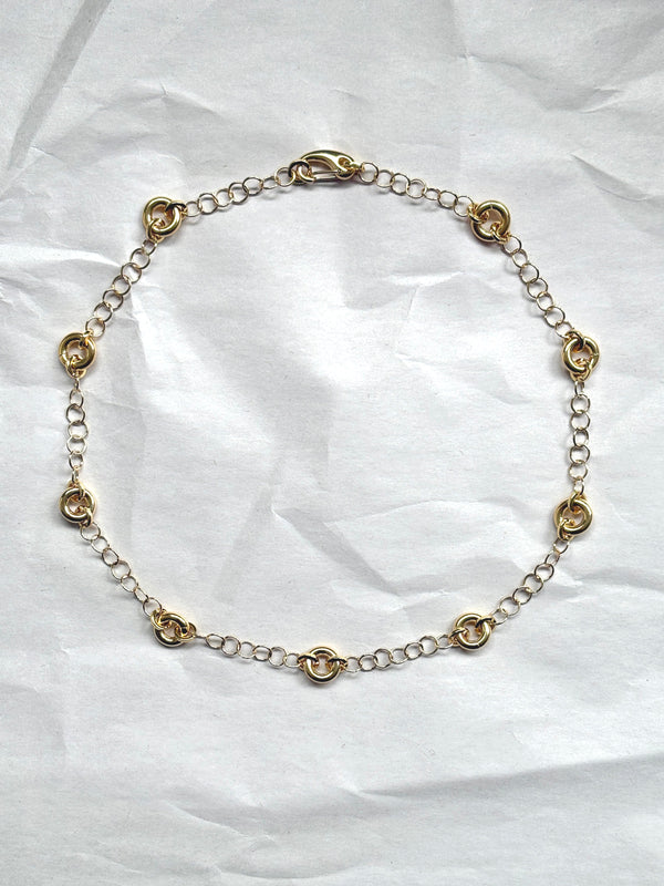 Delicate gold cable chain necklace with circular link accents, laid flat on a neutral background.