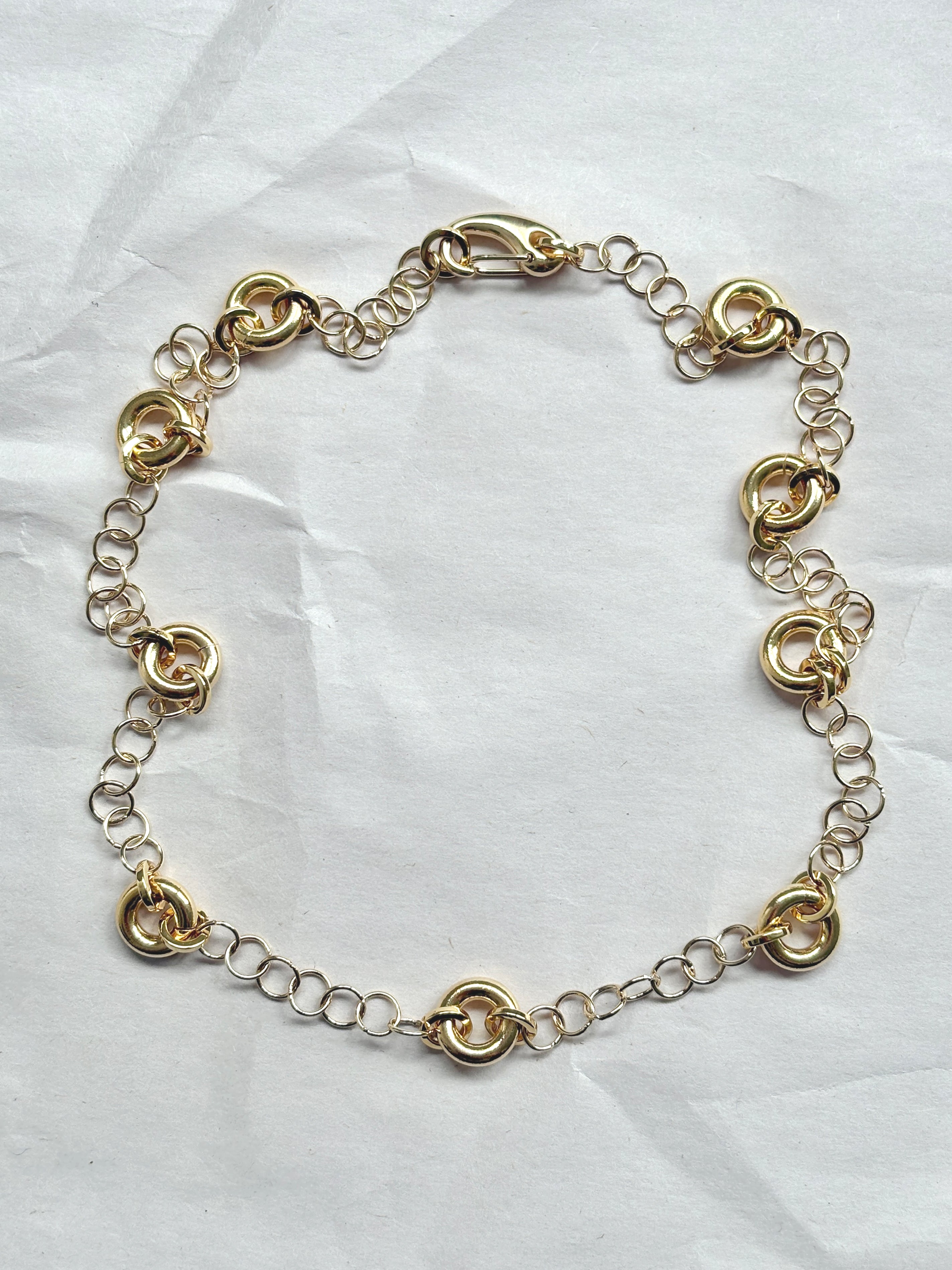 Delicate gold cable chain necklace with circular link accents, laid flat on a neutral background.