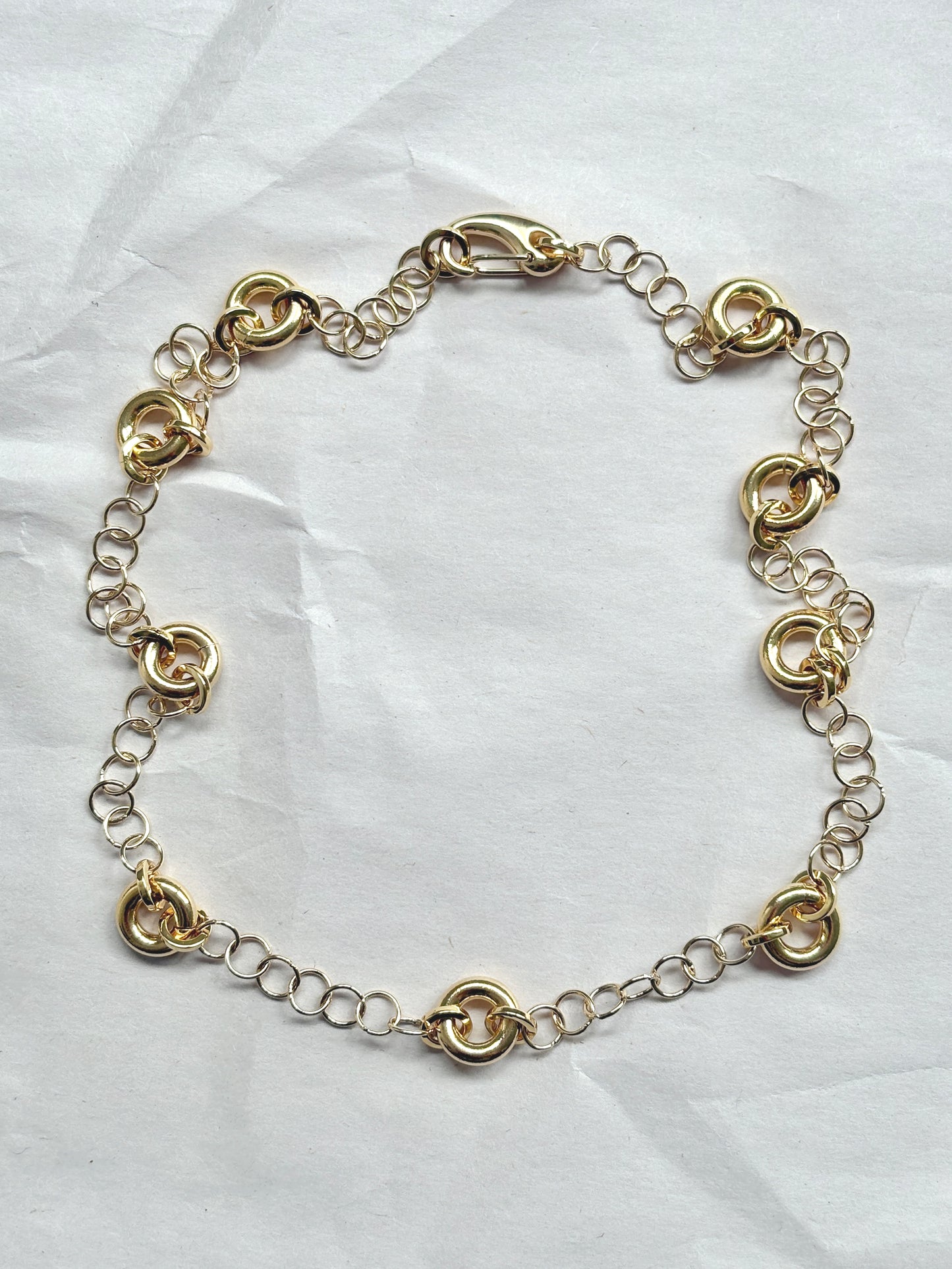 Delicate gold cable chain necklace with circular link accents, laid flat on a neutral background.