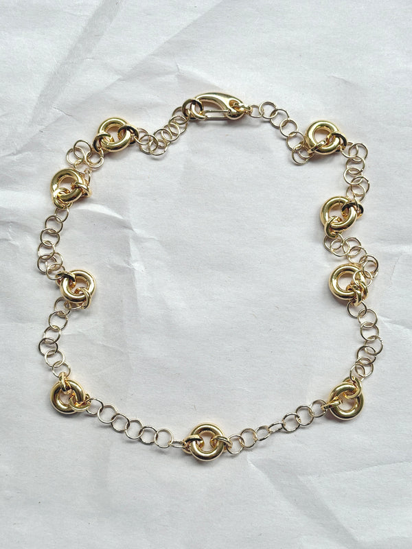 Delicate gold cable chain necklace with circular link accents, laid flat on a neutral background.