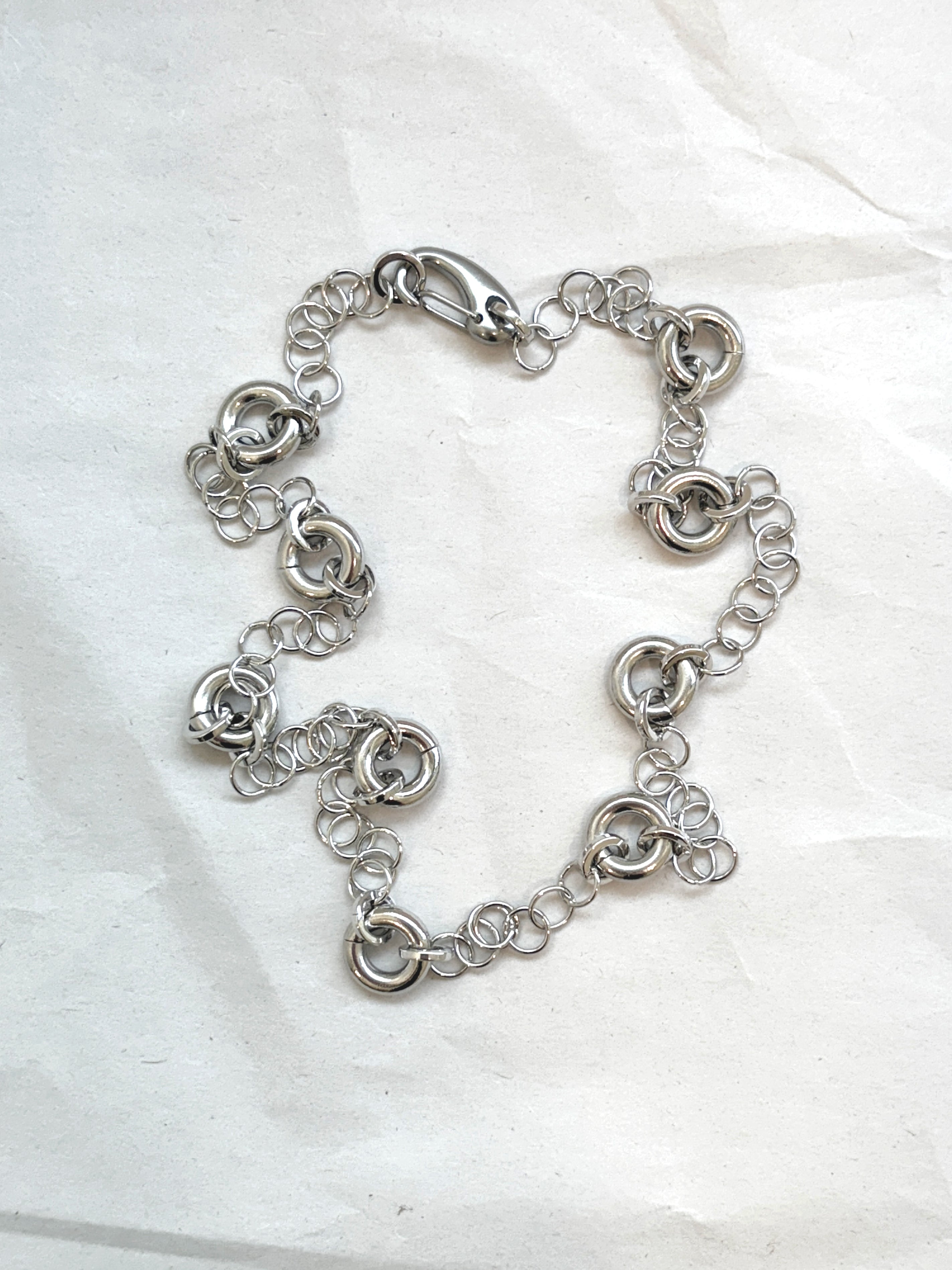 Delicate silver cable chain necklace with circular link accents, laid flat on a neutral background.