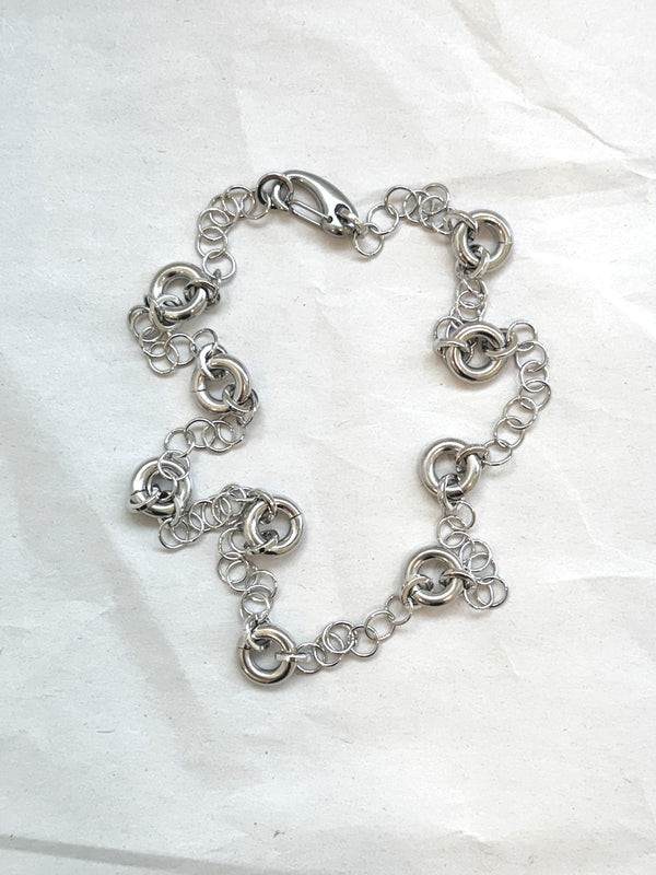 Delicate silver cable chain necklace with circular link accents, laid flat on a neutral background.