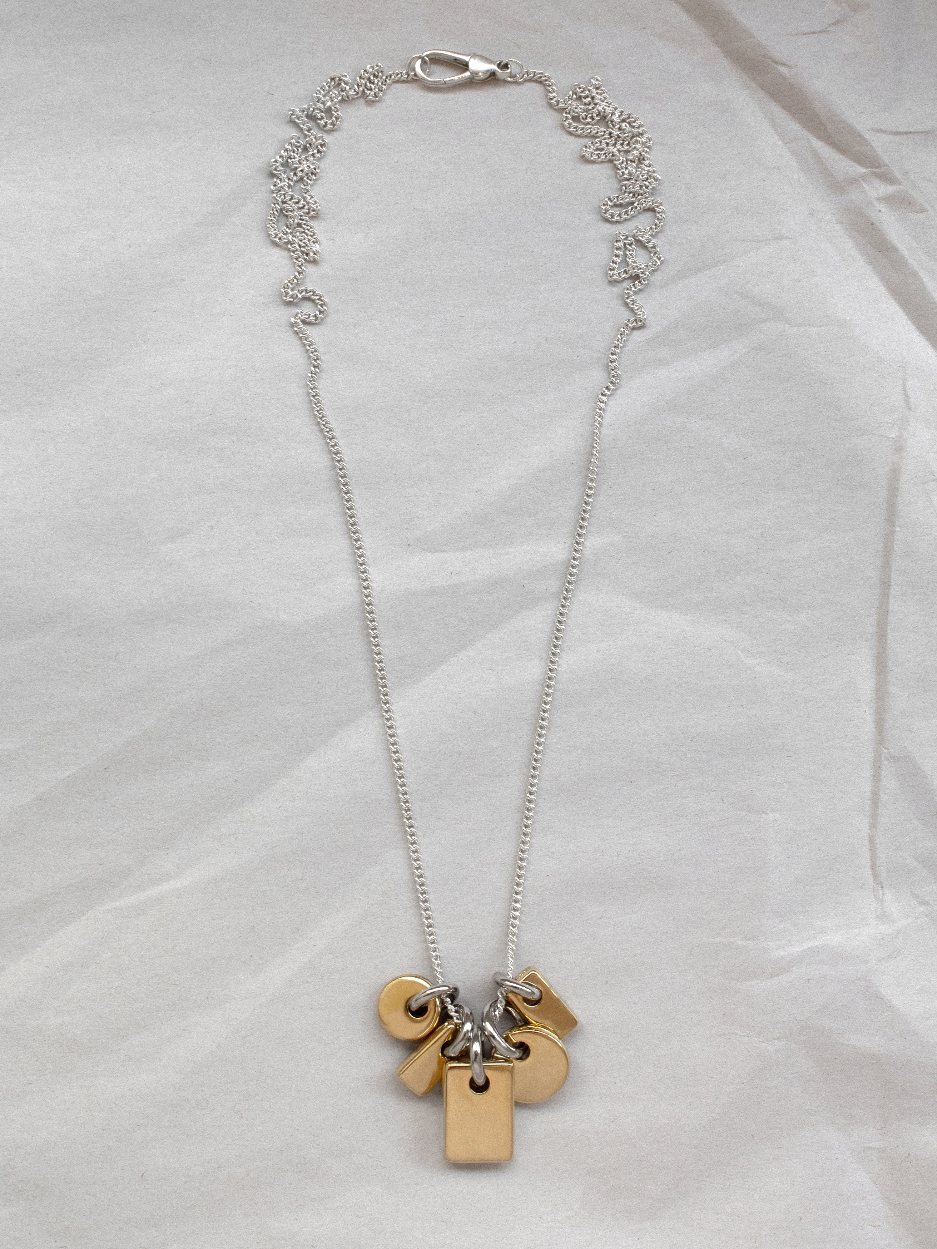 Necklace with gold and silver pendants on a sterling silver chain laid flat on a paper background.