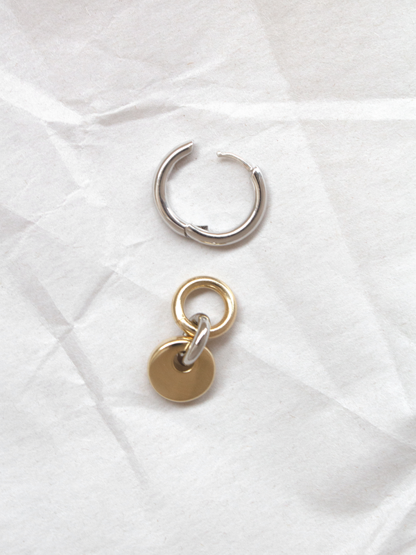 A single silver hoop with removable gold circular charm shown separately, laid flat on a paper background.
