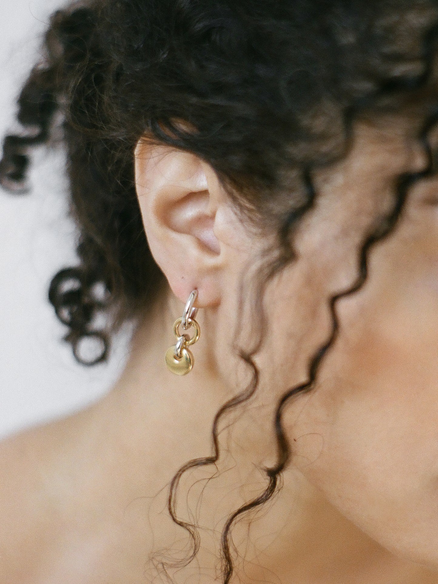 Model wearing a pair of silver hoops with gold rectangular charms on a neutral background.