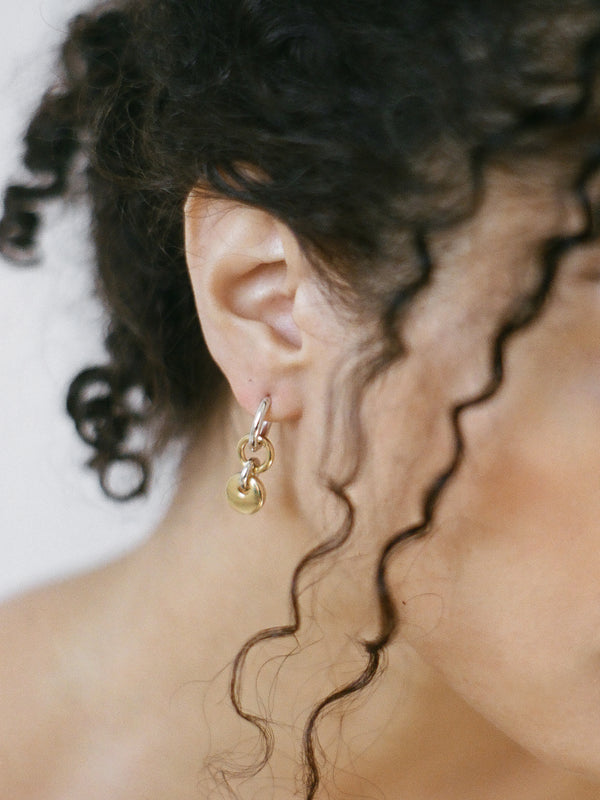Model wearing a pair of silver hoops with gold rectangular charms on a neutral background.