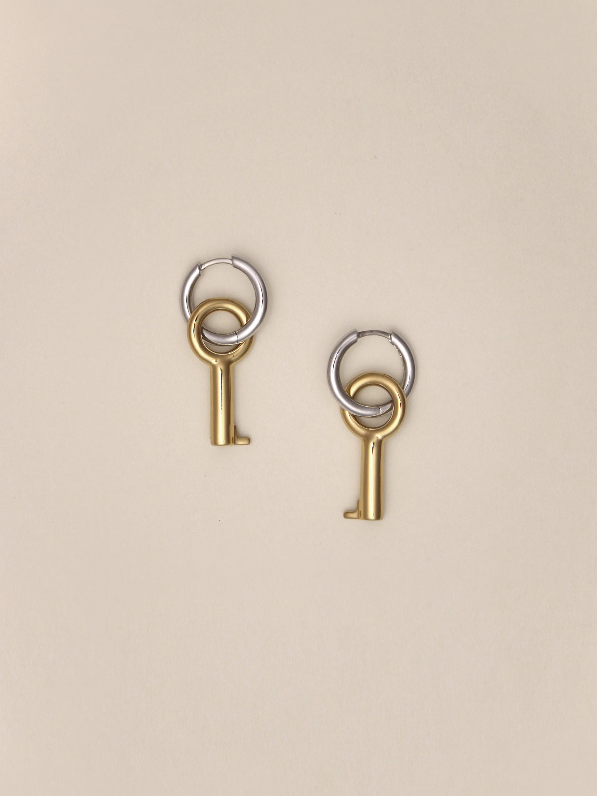 Laura Lombardi Two Tone Entra Earrings, a pair of petite silver hoop earrings with dangling gold key charms, shown on a neutral background.