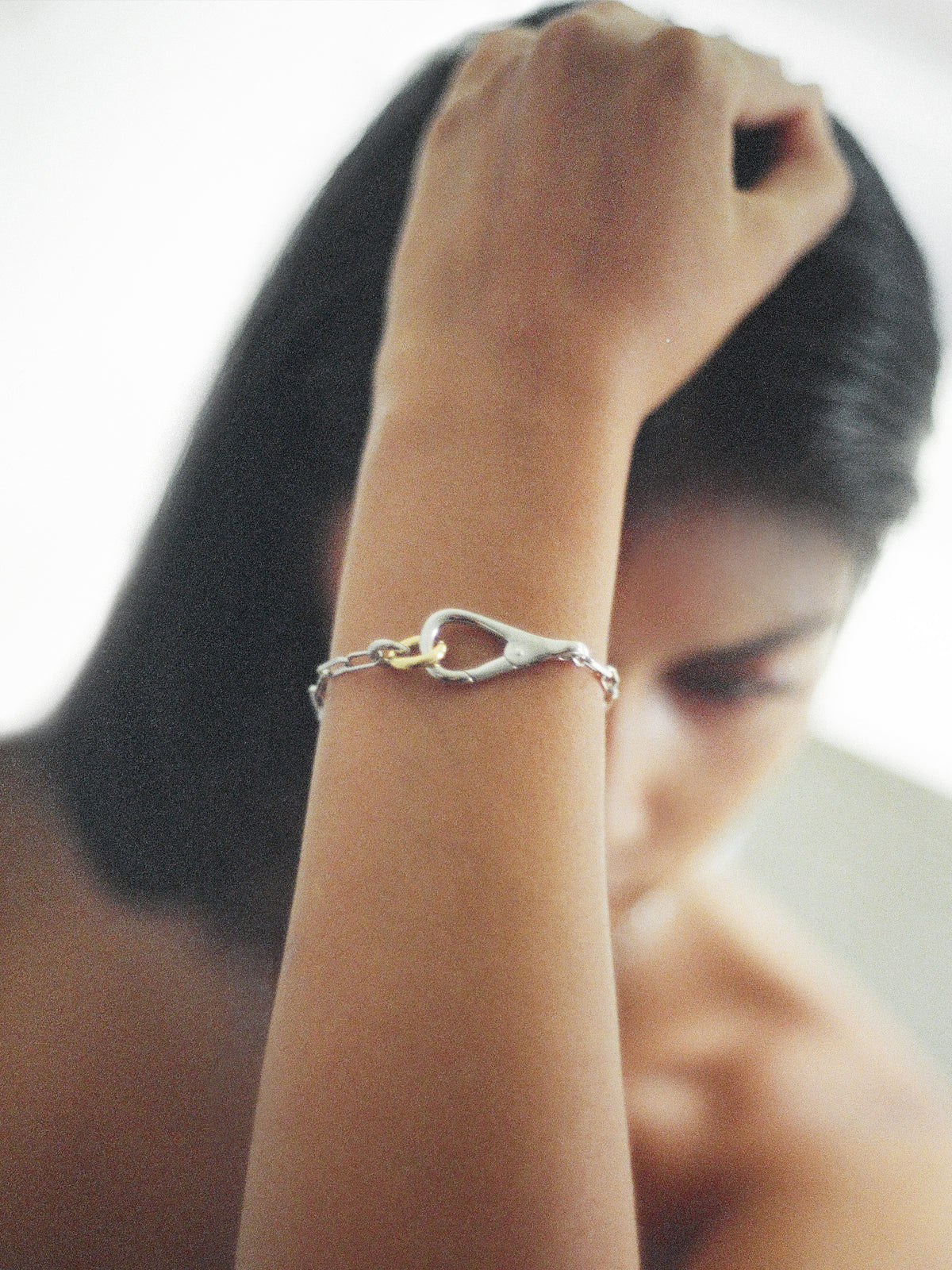 Model wearing the Two Tone Frena Bracelet, a silver-toned chain bracelet with a silver toggle clasp and gold jump ring, displayed on a neutral background.