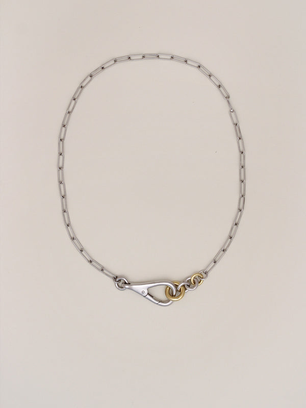 Two Tone Frena Necklace, a silver-toned oval chain necklace with a silver toggle clasp and gold jump ring, displayed on a neutral background.