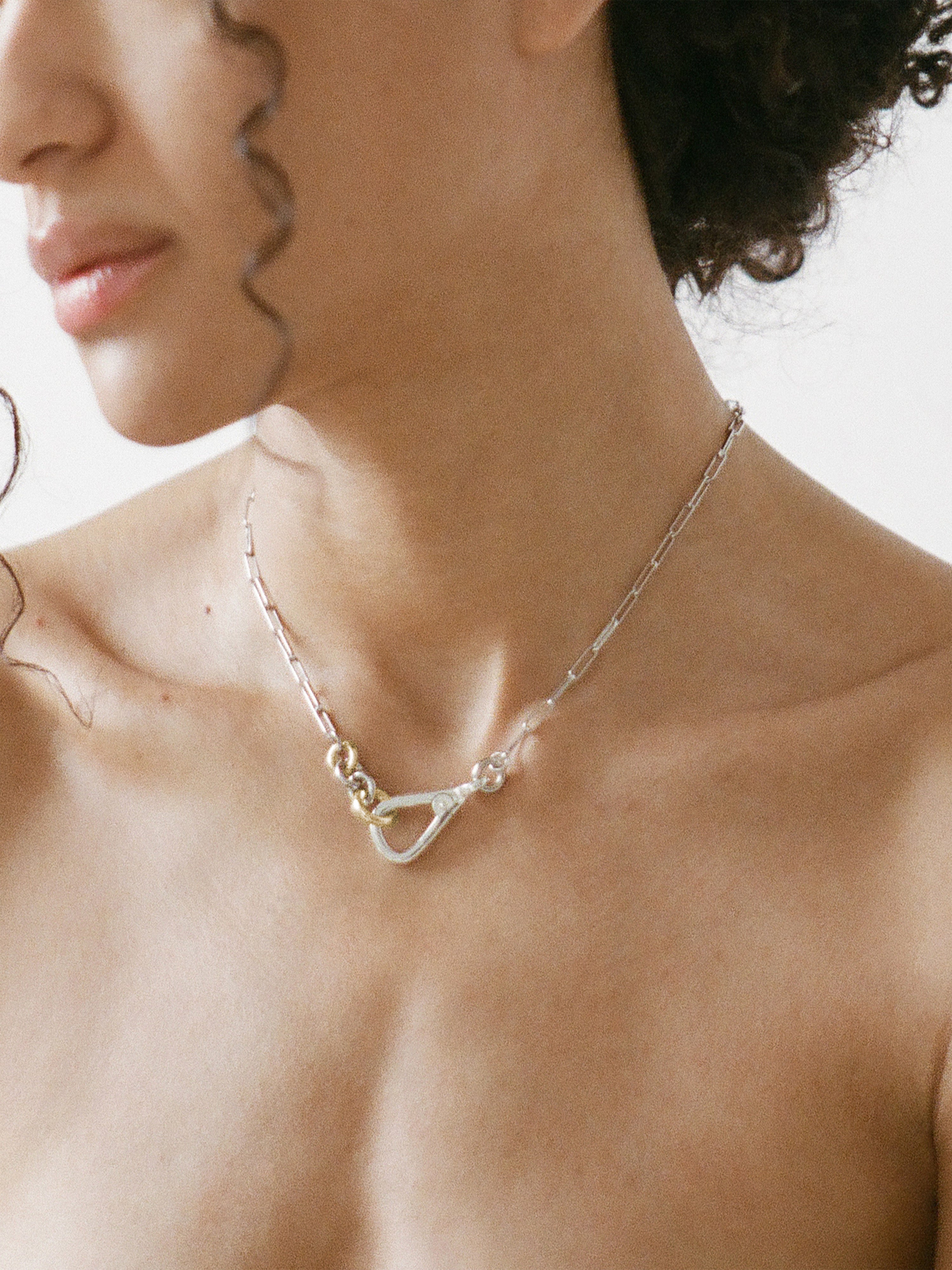 Two Tone Frena Necklace, a silver-toned oval chain necklace with a silver toggle clasp and gold jump ring, displayed on a neutral background.
