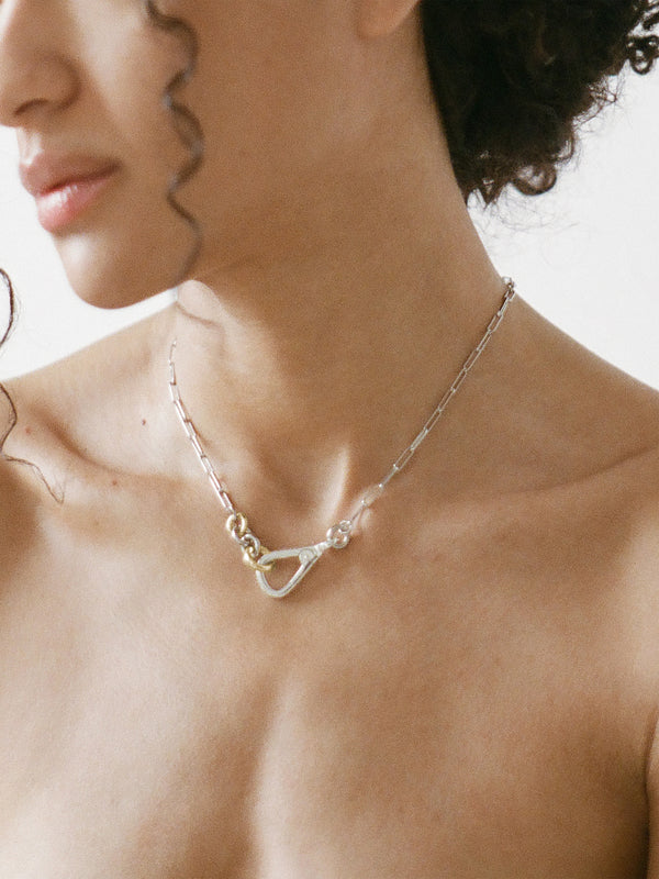 Model wearing the Two Tone Frena Necklace, a silver-toned oval chain necklace with a silver toggle clasp and gold jump ring, displayed on a neutral background.