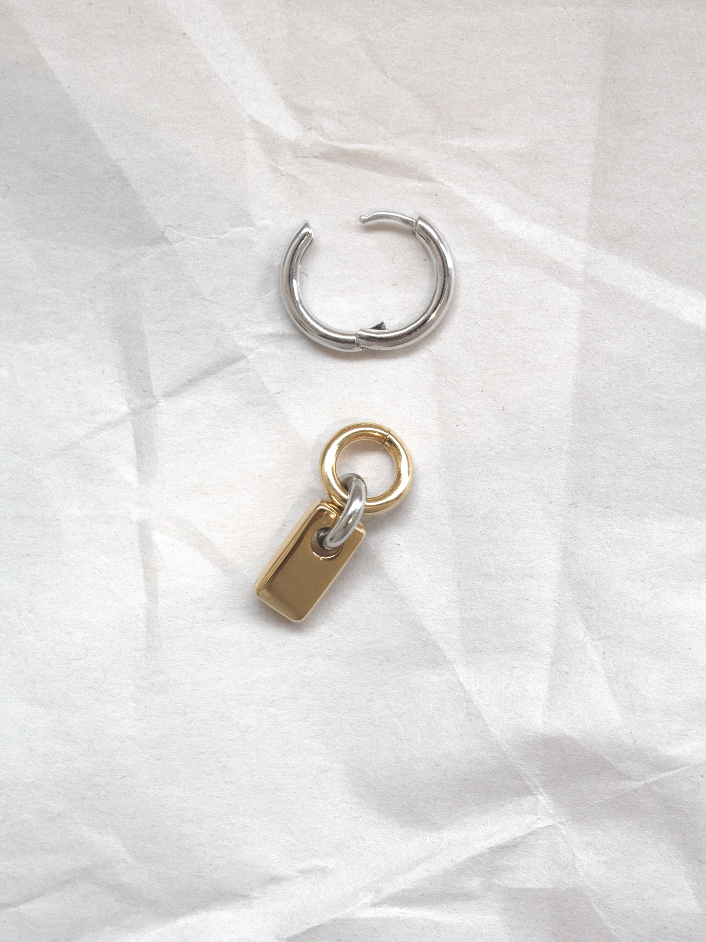 A single silver hoop with removable gold rectangular charm shown separately, laid flat on a paper background.