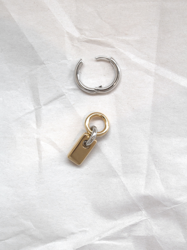 A single silver hoop with removable gold rectangular charm shown separately, laid flat on a paper background.