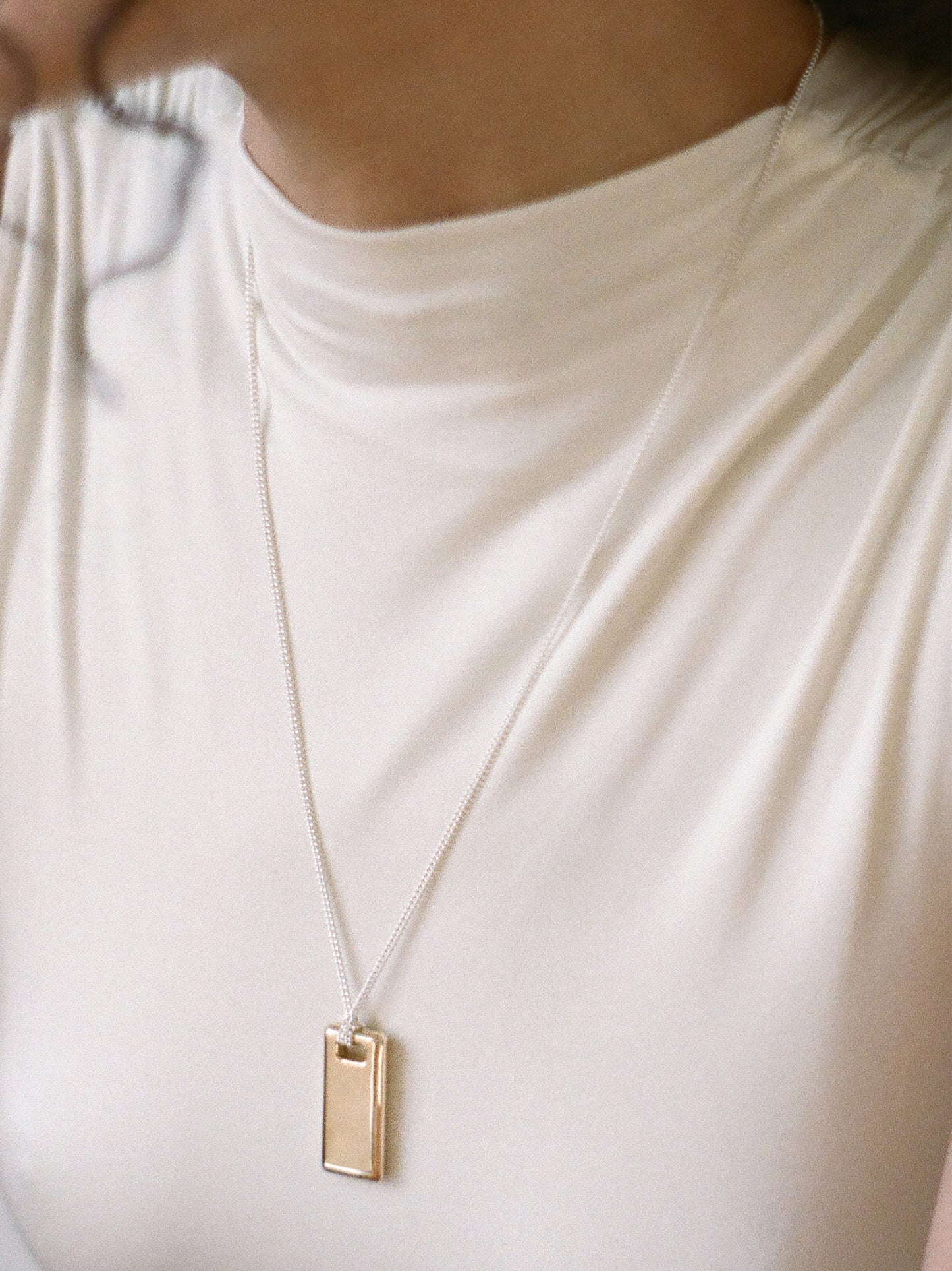 Model wearing a gold rectangular pendant on a sterling silver chain against a neutral background.