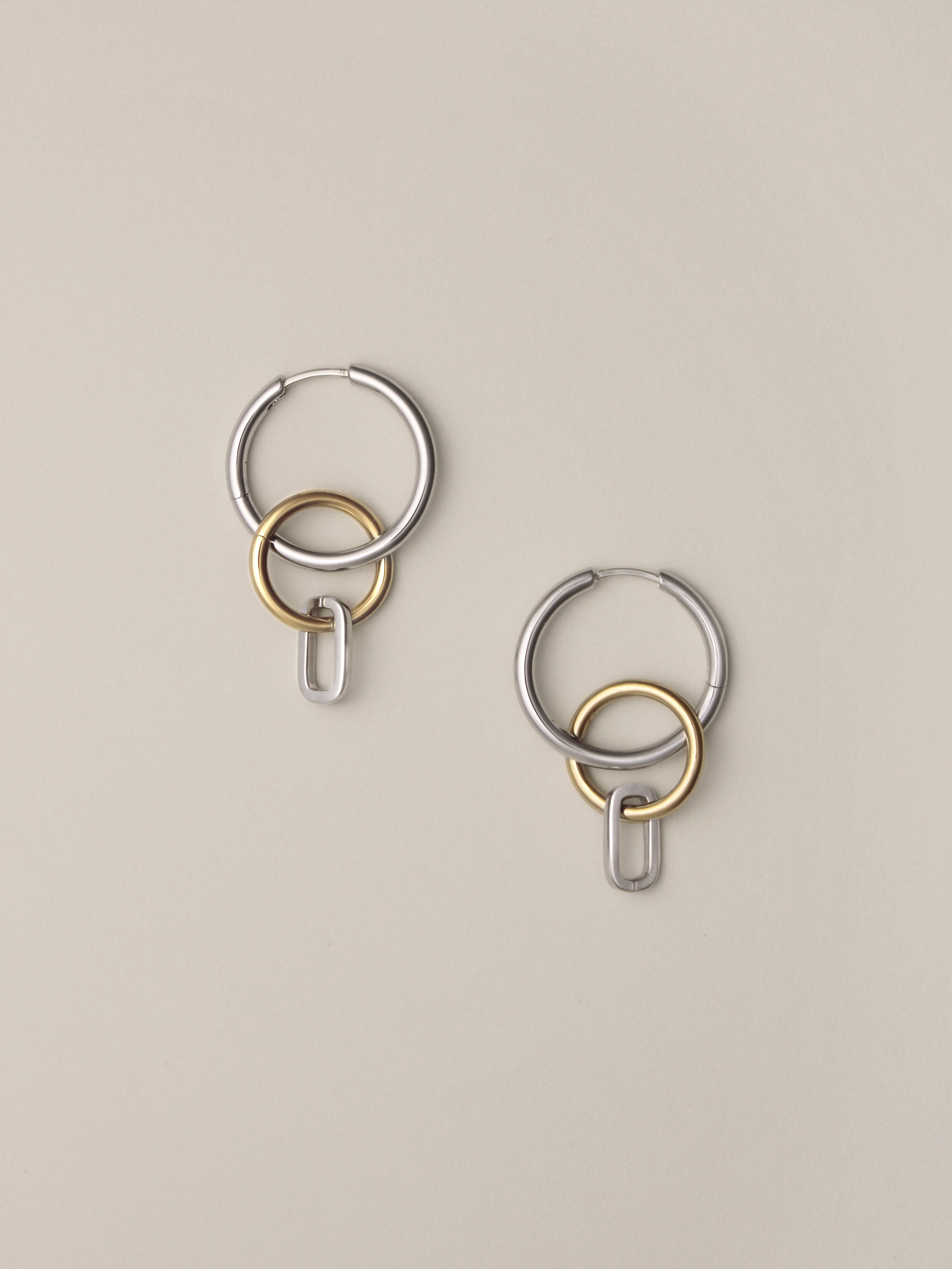 Side view of Laura Lombardi Two Tone Passa Earrings, medium silver hoops with a gold circular charm and a silver oval charm.