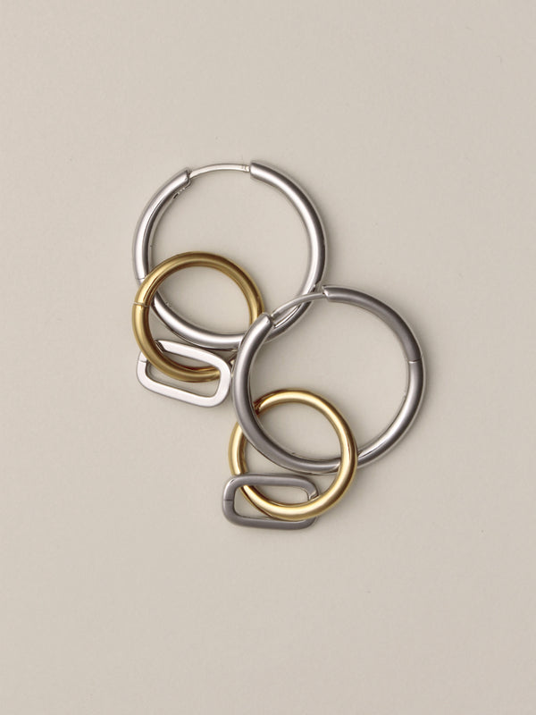 Laura Lombardi Two Tone Passa Earrings, medium silver hoops with a gold circular charm and a silver oval charm, layered on top of eachother.