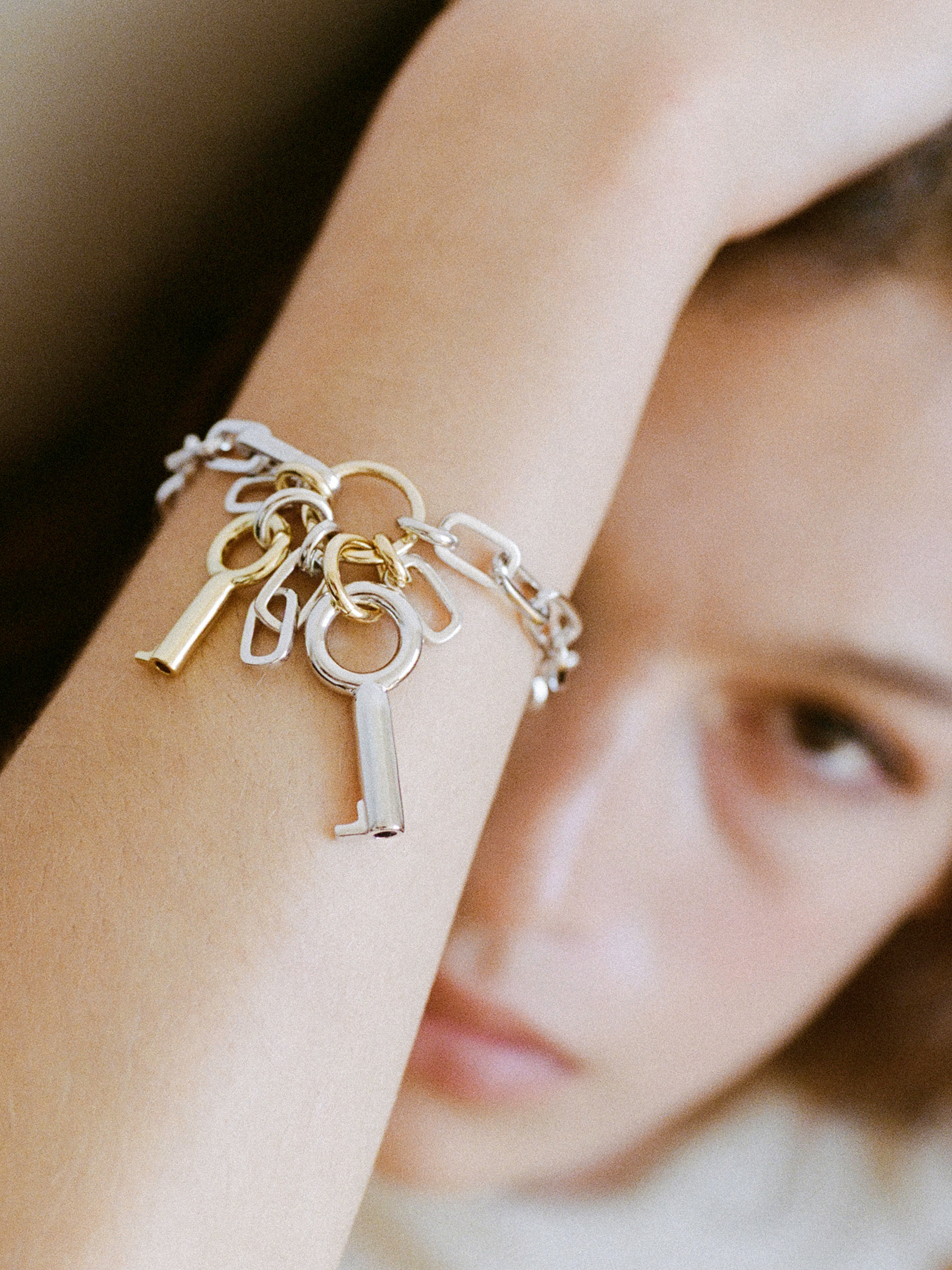Laura Lombardi Permesso Bracelet, a silver chain bracelet with hanging keys and  chains in mixed silver and gold finishes, isolated on a white background.