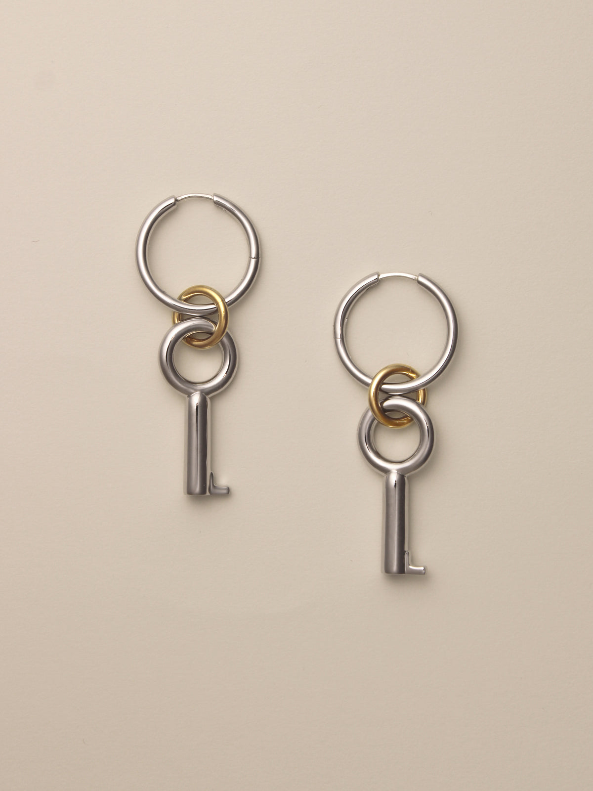The Two Tone Permesso Earrings, a pair of silver hoop earrings with key-shaped charms and small gold rings connecting the hoops, shown on a neutral background.