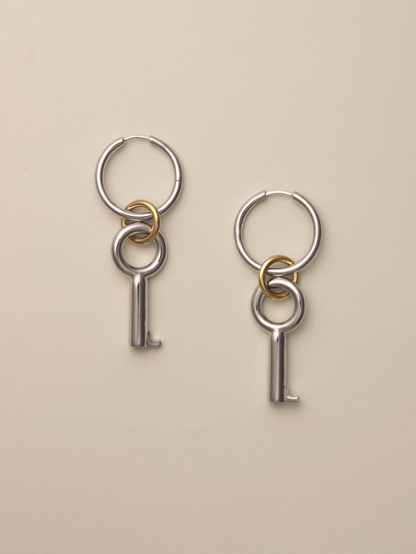 The Two Tone Permesso Earrings, a pair of silver hoop earrings with key-shaped charms and small gold rings connecting the hoops, shown on a neutral background.