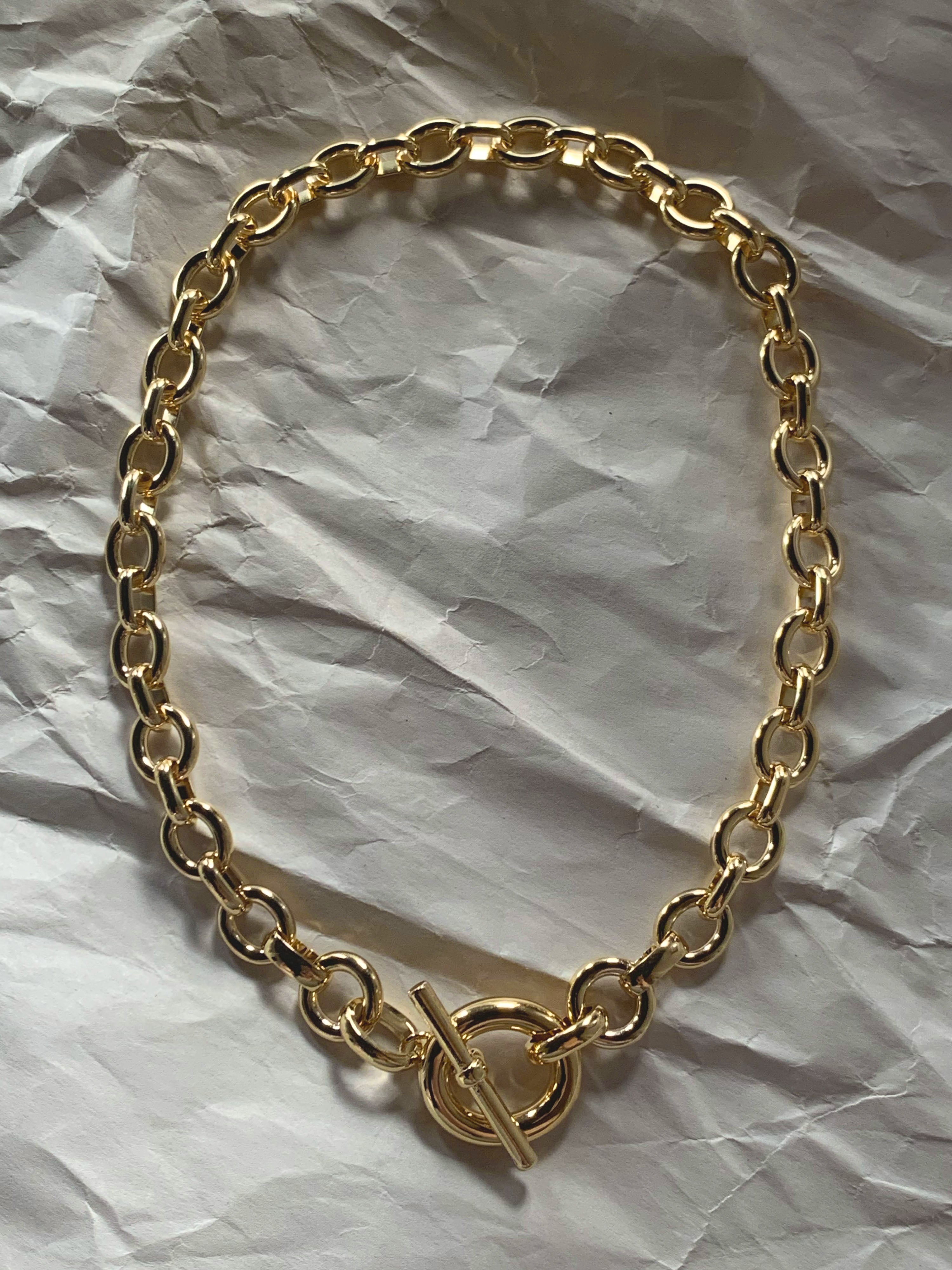Gold chain necklace with a toggle clasp laid flat on paper.