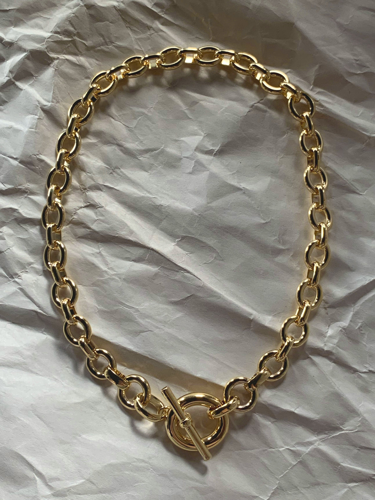 Gold chain necklace with a toggle clasp laid flat on paper.