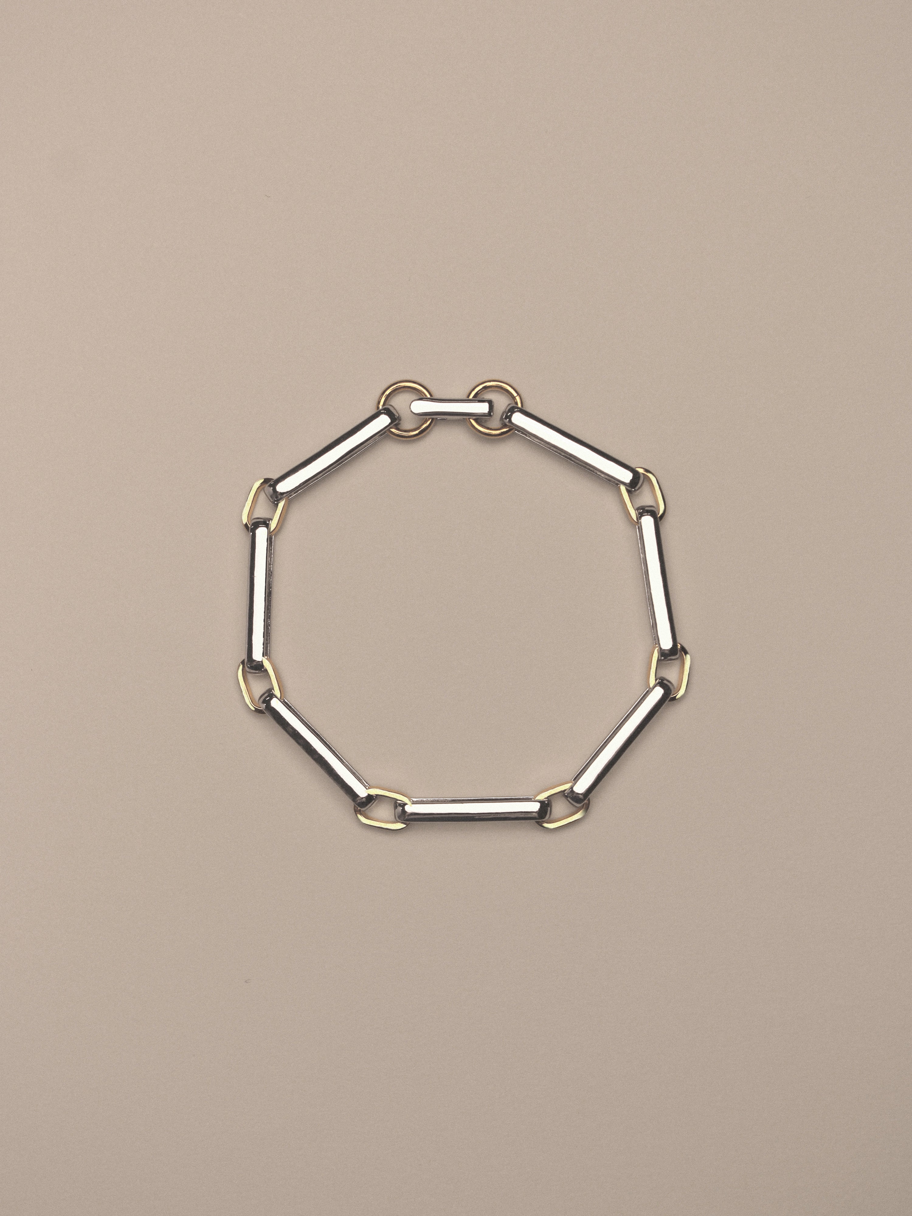 A two-tone chain link bracelet featuring silver-toned rectangular links and gold-toned square accents,  shown on a neutral beige background.