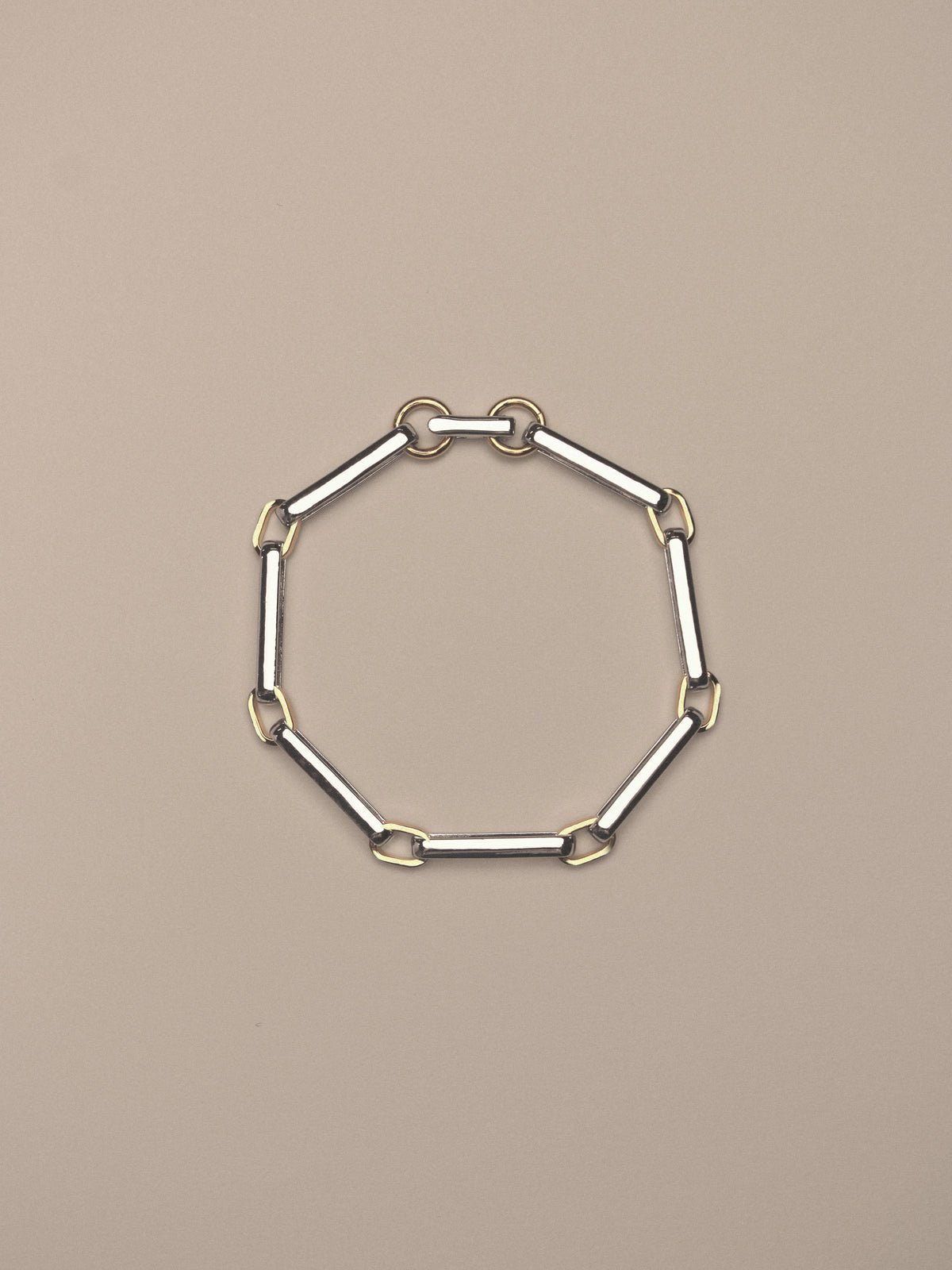 A two-tone chain link bracelet featuring silver-toned rectangular links and gold-toned square accents,  shown on a neutral beige background.