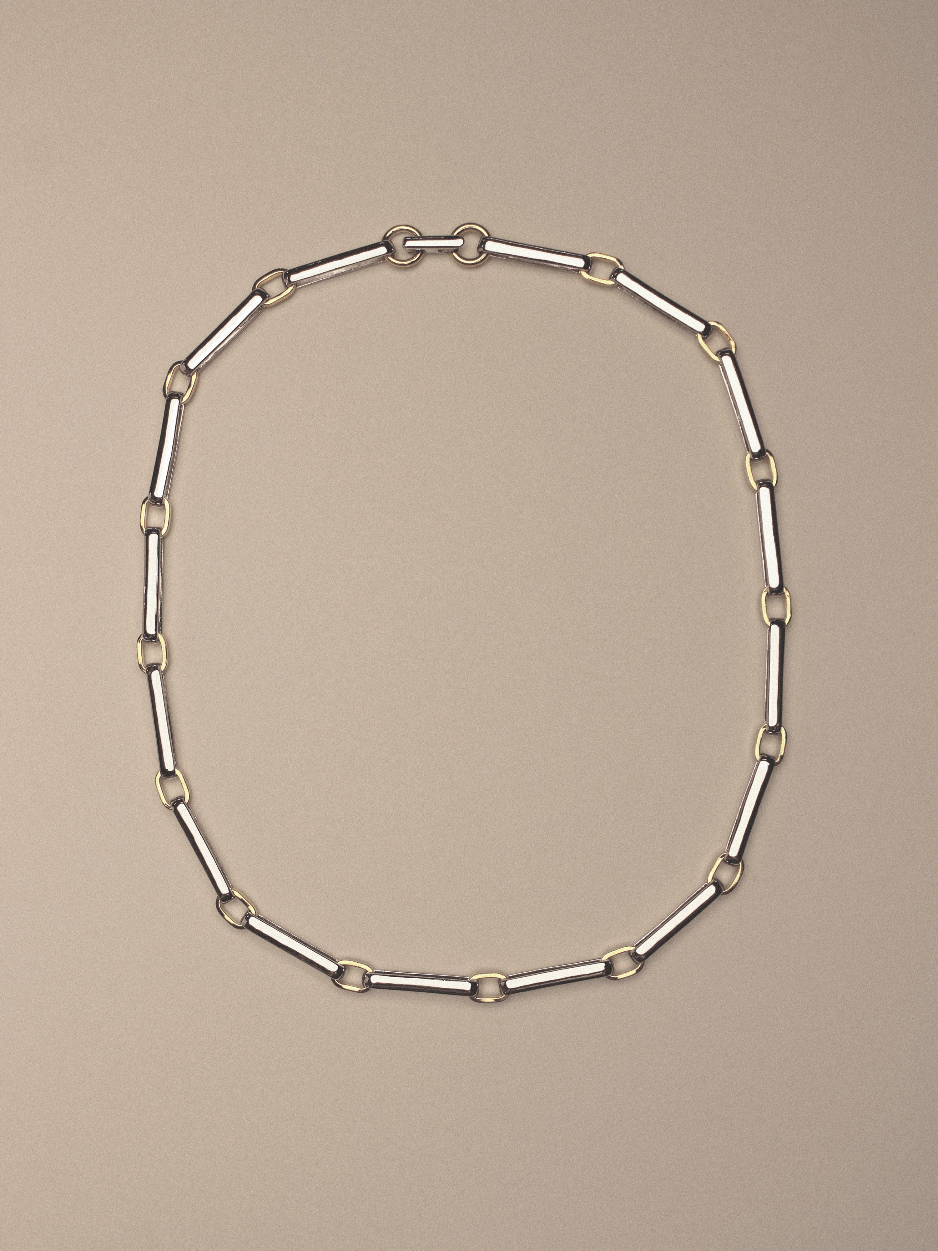 A two-tone chain link necklace featuring silver-toned rectangular links and gold-toned square accents,  shown on a solid beige background.
