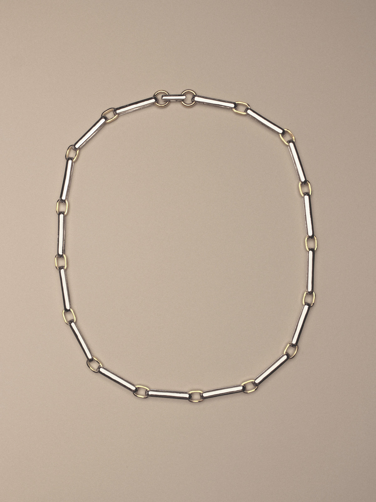 A two-tone chain link necklace featuring silver-toned rectangular links and gold-toned square accents,  shown on a solid beige background.