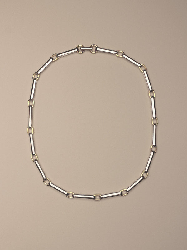 A two-tone chain link necklace featuring silver-toned rectangular links and gold-toned square accents,  shown on a solid beige background.